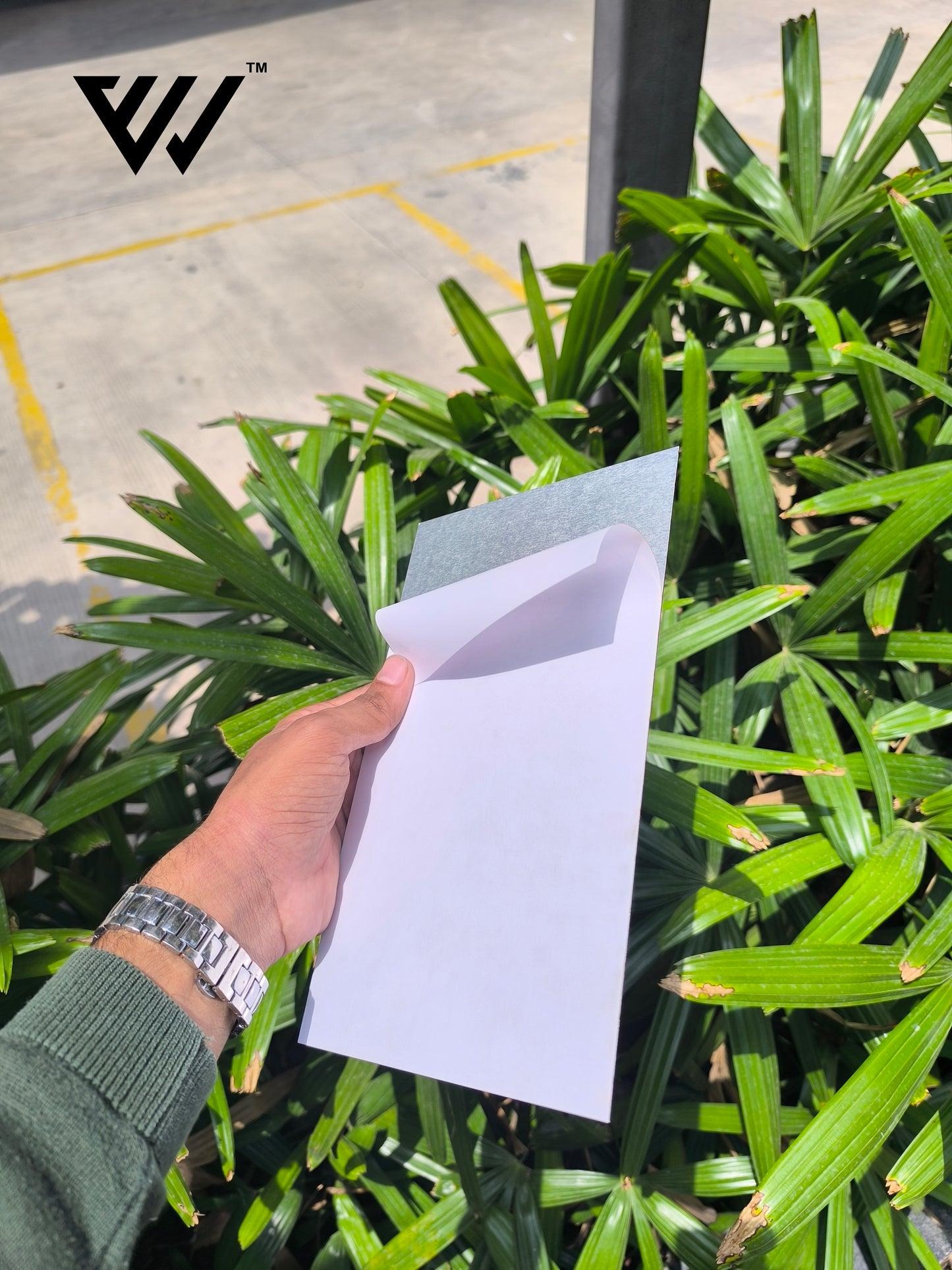 hand holding a white card in front of green plants with a brand logo in the corner.