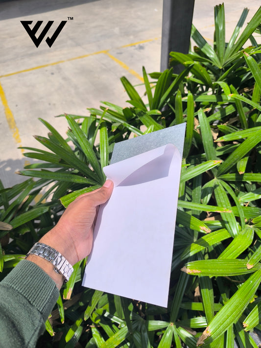 Hand holding a white card in front of green plants with a brand logo in the corner.